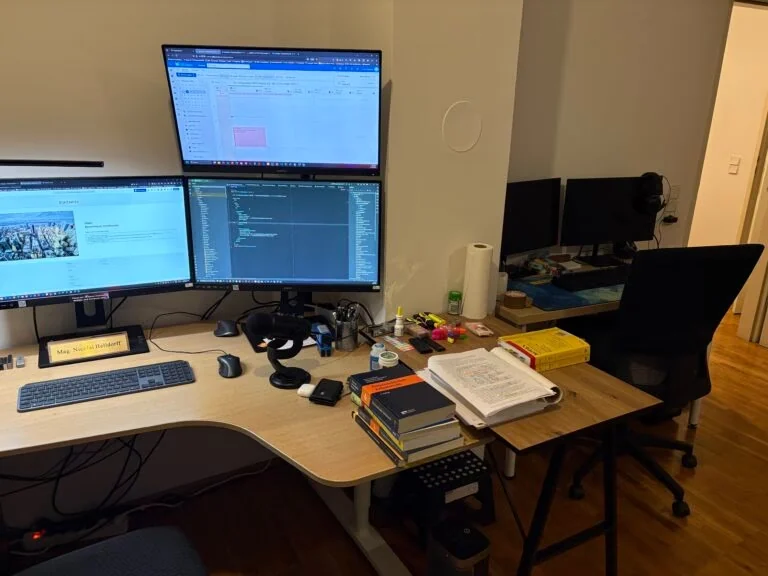 Arbeitsplatz von Ing. Mag. Nicolai Helldorff mit Monitoren, Code und juristischer Fachliteratur
